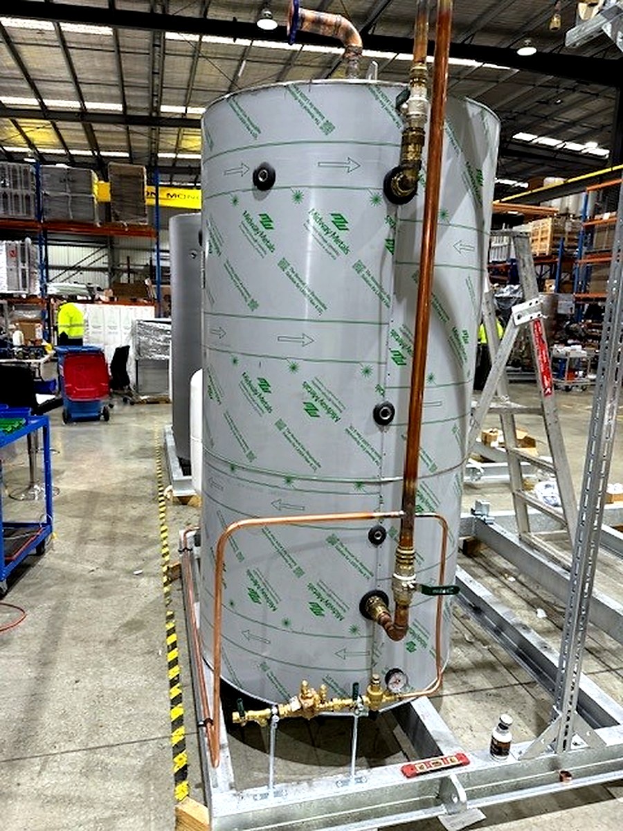 Sheet metal cladding material being applied to a cylindrical pressure vessel in a warehouse